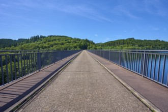 A straight view along a dam with a view of wooded land under a clear sky, Oleftalsperre,