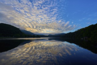 Peaceful morning atmosphere with dramatic sky reflected on the still lake, surrounded by green