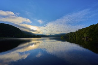 A tranquil lake reflecting dramatic sky and clouds offers a calming view with sweeping mountains,