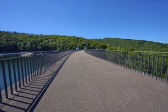 Straight view of an asphalted bridge with railing over a dam, summer, Urft dam wall, Obersee,