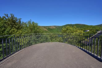 Viewing platform with railings in front of a wooded hilly landscape under a clear blue sky, summer,