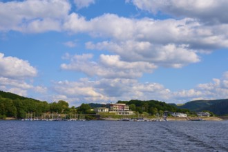 Buildings and boats along a lake in front of a sky with white clouds, summer, Rursee, Rurtalsperre,
