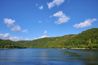 Calm lake surrounded by wooded hills under a clear, cloudy sky, summer, Rursee, Rurtalsperre,