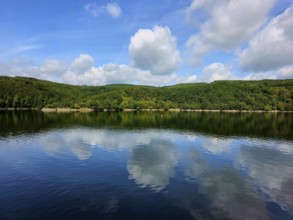 Clear blue sky with white clouds reflected in the still water of a lake and wooded shores, summer,