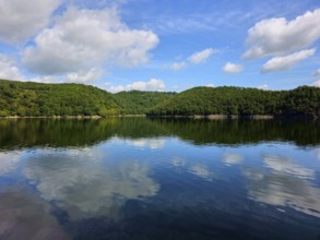 Blue sky with white clouds and their reflection in a calm lake, surrounded by lush forests, summer,