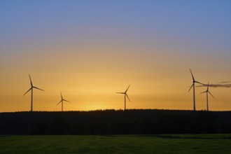 Wind turbines in front of an orange-coloured sky at sunrise, above a meadow, summer, Rohren,