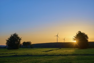 Wind turbines and trees at sunrise, the orange-coloured sky radiates warmth, summer, Rohren,