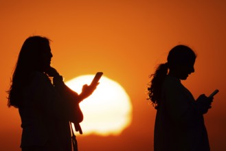 People photographing the sun setting on the horizon with their smartphones from the summit of the