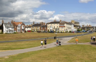 People walking on paths on grass area next to Queens Road, Southwold, Suffolk, England, Uk