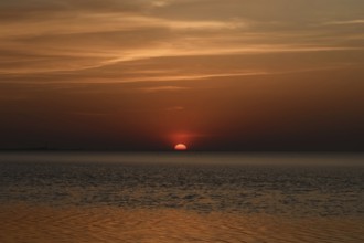Atmospheric sunset... Cuxhaven, North Sea, in calm weather, glowing red sun sinking into the sea,