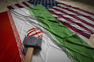 Large hammer, american and Iranian flags resting on desert sand