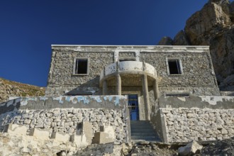 Old stone house against an imposing rocky backdrop, historic and sunlit, Embros Thermal Baths, Kos,