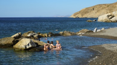 People relaxing in the water on the coast with rocks and clear blue sea, Embros Thermal Baths, Kos,