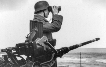 German WWII soldier looking over the North Sea with binoculars next to anti-aircraft gun at WW2