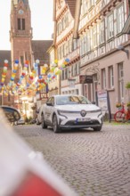 A white electric car parked on a cobbled street decorated with balloons in the old town centre,