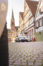 A car drives through a historic town with half-timbered houses and balloons, Deer E, car sharing,