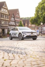 A white car parked on a cobbled square with charming half-timbered houses in the background, Deer