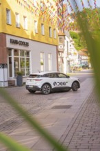 A car parked on a cobbled street with colourful houses, Deer E, car sharing, electric car, Calw,