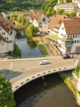 A car drives over a bridge that crosses a river in a charming urban landscape with green