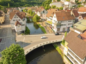 Aerial view of a town with a river and bridge, showing half-timbered buildings and green trees from
