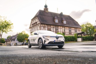 A white electric car drives past a traditional building in a historic town, Deer E, car sharing,