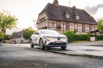 An electric car in an old town centre with a historic building in the background, streets wet, Deer
