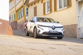 A white car on a street in a historic town with half-timbered houses, Deer E, car sharing, electric