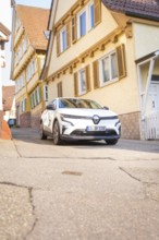 A white car drives down a traditional street with half-timbered houses, Deer E, car sharing,