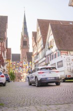 A car drives in an old town with colourful garlands in front of a church, Deer E, car sharing,