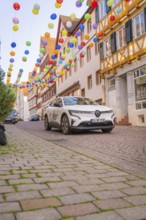 A car drives under colourful garlands in a cobbled street, Deer E, car sharing, electric car, Calw,