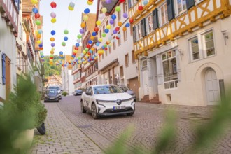 A car drives through a street decorated with colourful garlands in an old town, Deer E, car