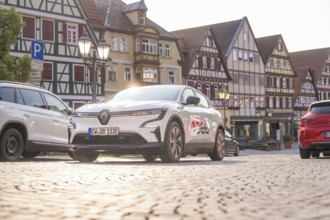A car parked on cobblestones in the low sunlight, surrounded by half-timbered houses, Deer E, car