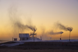 Snow cannons blow clouds of smoke on a hilltop under the purple twilight sky, winter, Route de