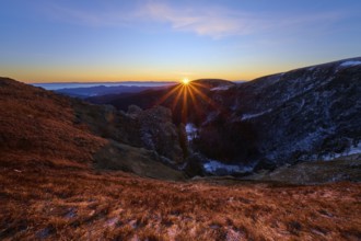 Sunbeams break over the mountains, orange sky and shades of blue, looking towards the Rhine Valley,