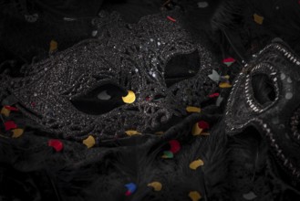 Black mask with confetti on dark background, contrasting carnival atmosphere