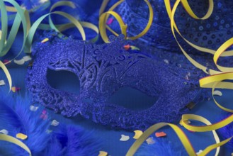 Blue mask with feathers, confetti, streamers and hat on blue background, carnival