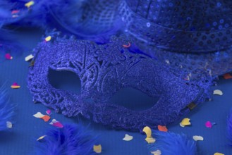 Blue mask with feathers, confetti and hat on blue background, carnival