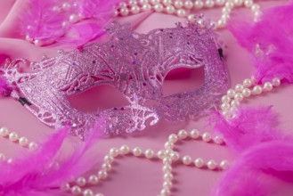 Glittering pink mask on pink background with feathers and pearl necklaces