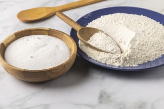 Flour and sugar in bowls with a wooden spoon on a marble plate