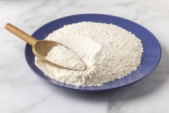 A blue plate with a large amount of flour and a wooden spoon