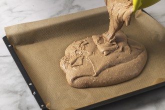 Cocoa dough is poured onto a baking sheet lined with baking paper