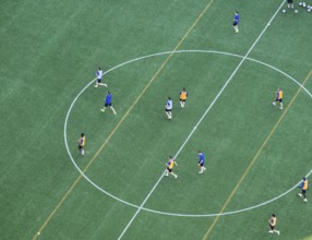Players wearing colorful jerseys play soccer on a grass field from a bird's eye view from the tower