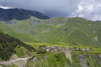 Mountain village in green hilly surroundings under a cloudy sky, dramatic landscape, view of
