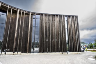Detailed view of a modern wooden façade with large glass windows under a cloudy sky, Sámi Cultural