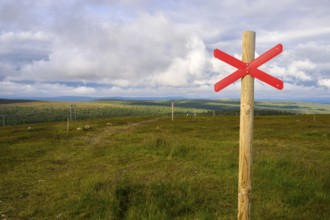 Red snowmobile snowscooter marker on a wooden post in front of a vast landscape under clouds,