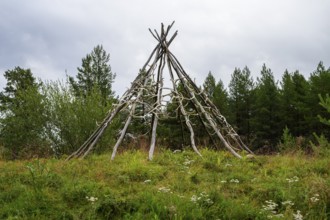 Rustic wooden structure made from birch trunks and reindeer antlers in a natural setting with trees