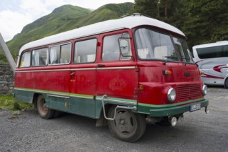 Old nostalgic bus in red with green accent on a parking lot in a mountainous landscape, vintage