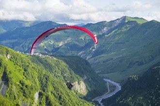 A paraglider floats over a lush green gorge with a winding river, paraglider, paraglider near