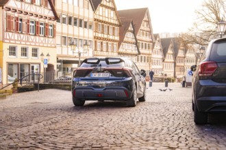 Back end of a car on a paved street surrounded by half-timbered houses in an old town, MG4 electric