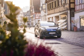 Black car in a charming old town, flowers in the foreground, morning atmosphere, MG4 electric car,